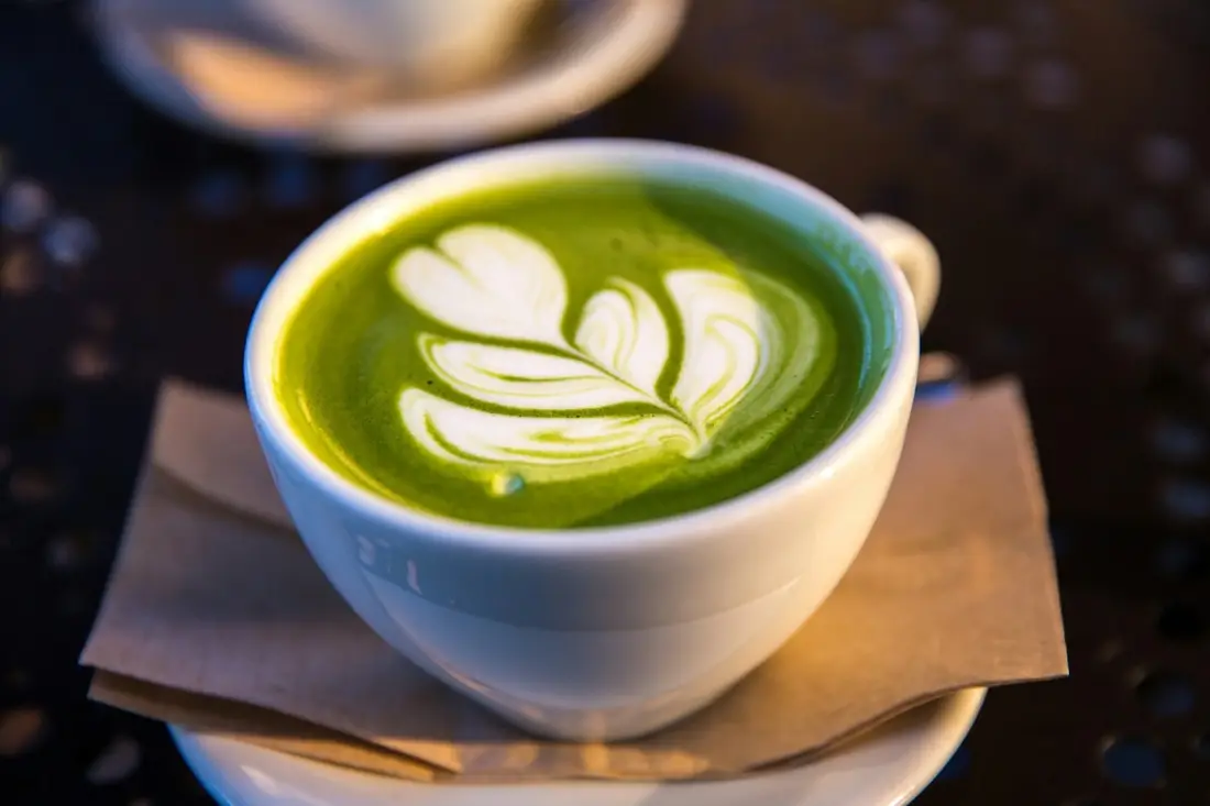 A matcha latte in a white cup, poured with a leaf pattern in the foam.