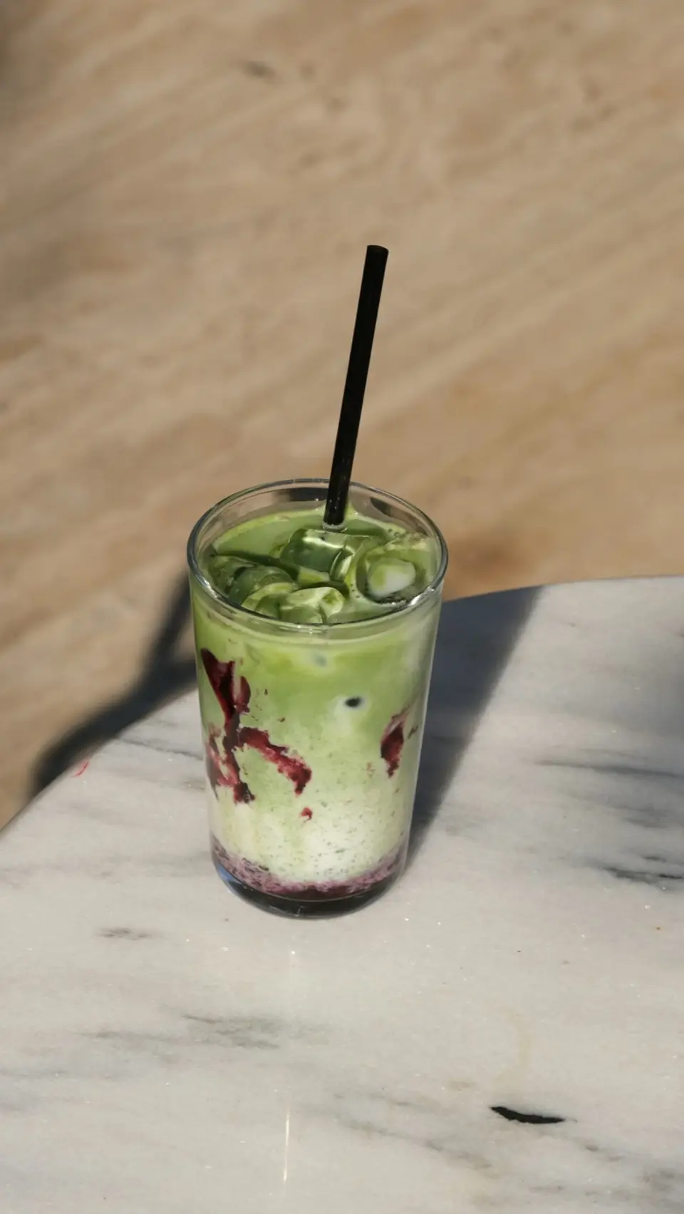An iced matcha in a tall glass with a straw, the milk and tea not yet stirred together.